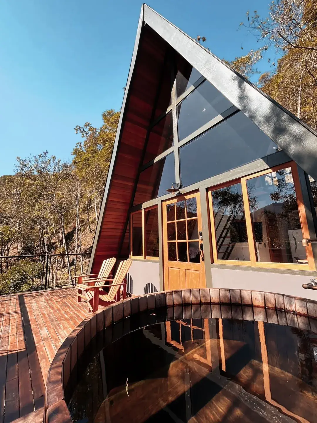Fachada A-frame refletida na água do ofurô, sob luz dourada de fim de tarde